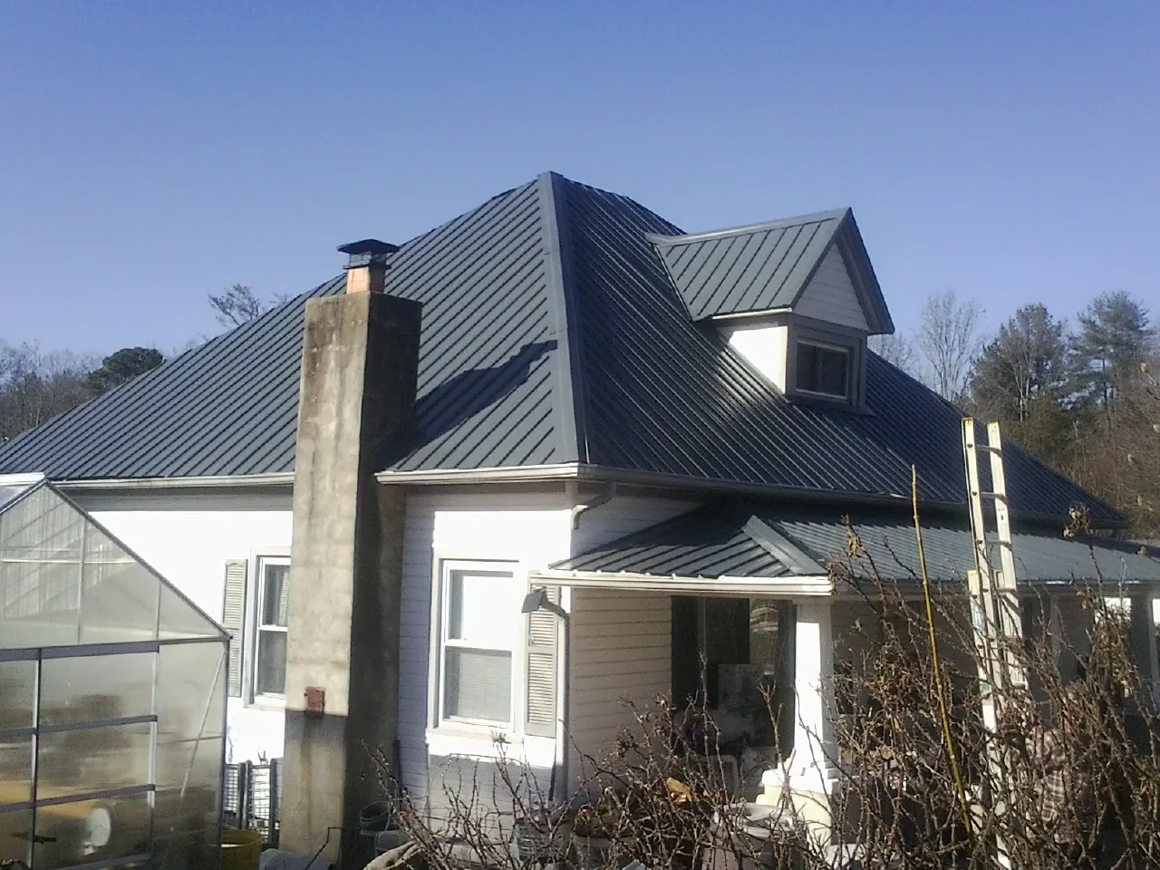 Dark blue standing seam metal roof on a white farmhouse with dormer — Slate & Tile Roof Repair by Roofing Brothers in East Canaan