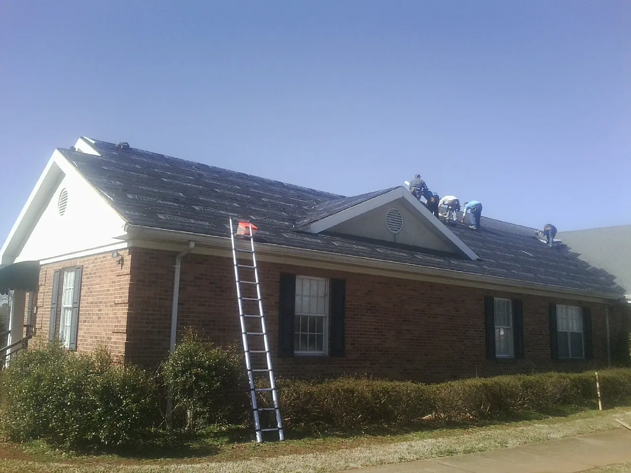 Crew tearing shingles off a brick ranch roof with a ladder set — Emergency Roof Repair work by our crew in East Canaan