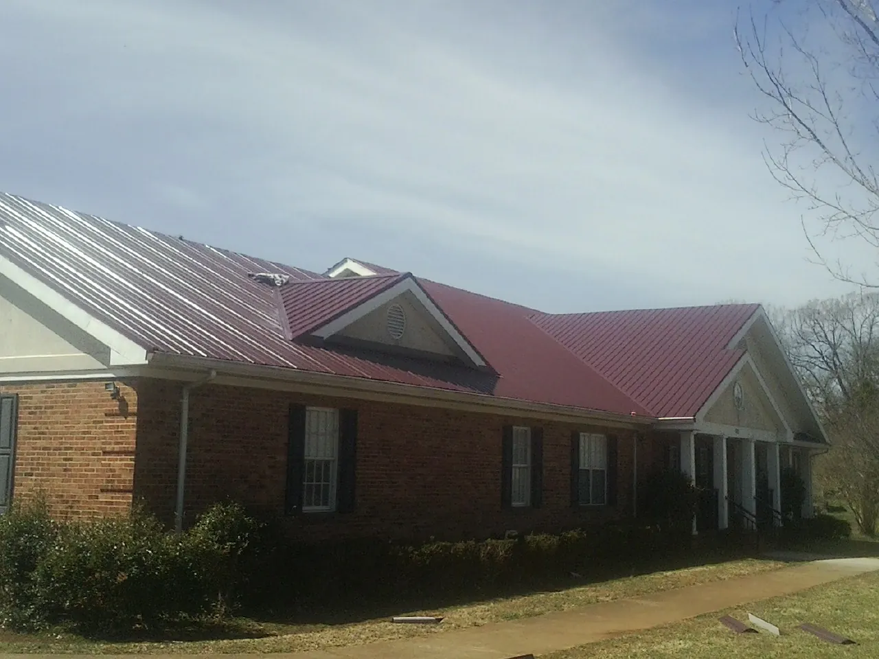 Red metal roof with gabled entries on a long brick building, from a Hail Damage Roof Repair job in East Canaan