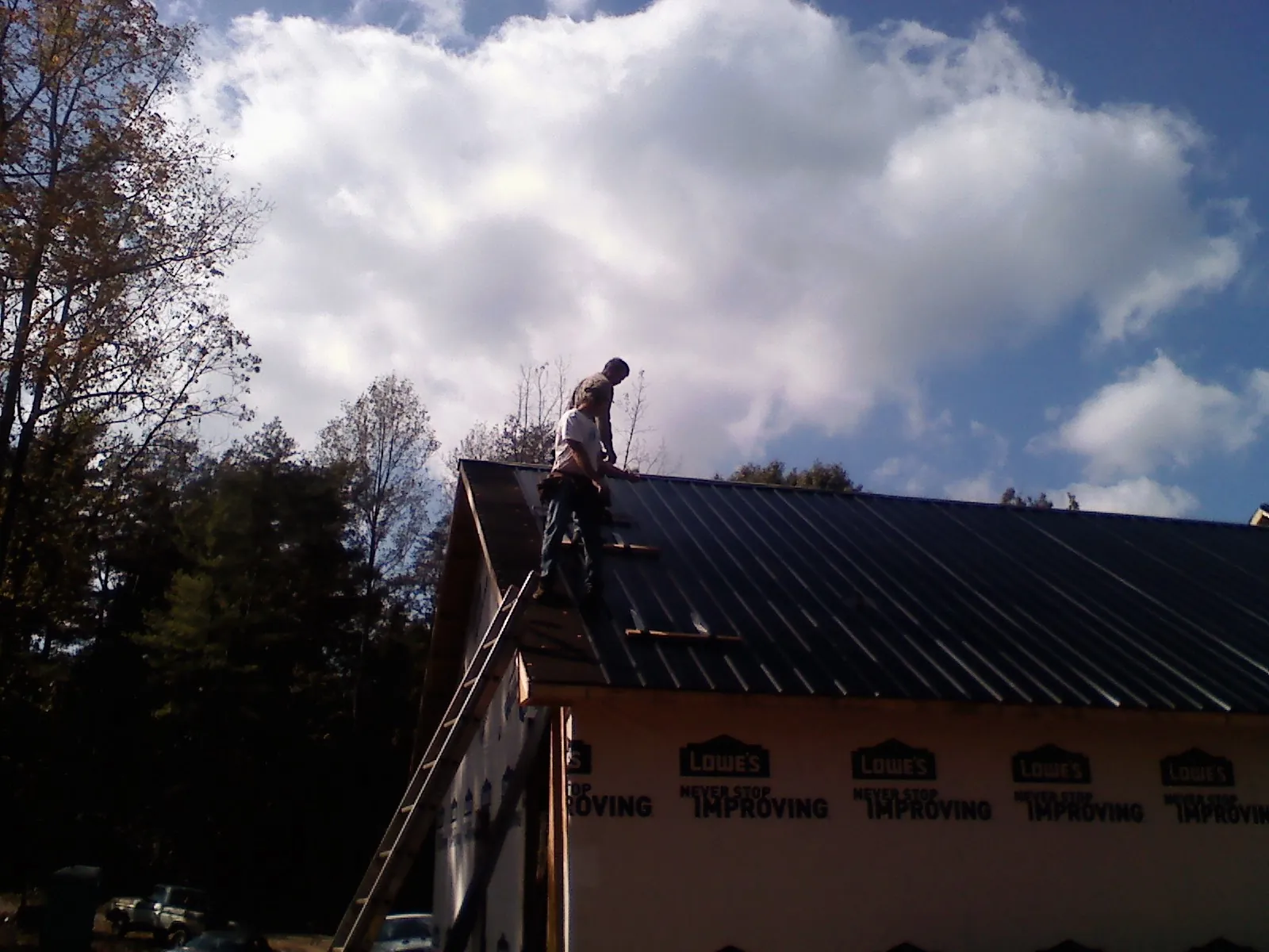 Roofer fastening dark metal panels high against a cloudy sky, from a Roof Inspection job in East Canaan