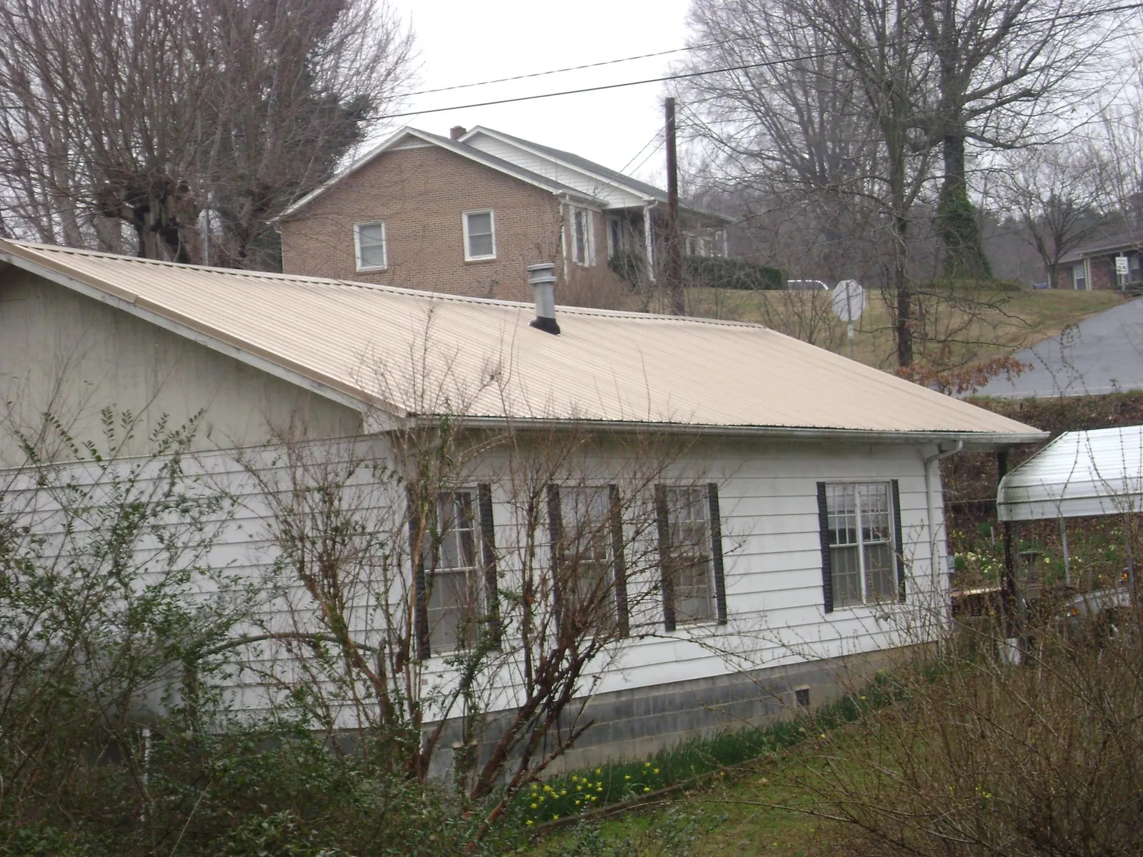Tan metal roof on a white sided house set into a hillside — Commercial Roofing by Roofing Brothers in East Canaan
